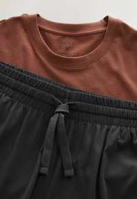 Brun bomulds T-shirt med rund hals, lagd over sorte shorts med snøre og en elastisk talje samt en glat tekstur.
