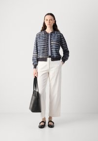 Strikket cardigan i marineblå og lyseblå med krave og knaplukning, parret med cremefarvede vide bukser og sorte lædertilbehør.