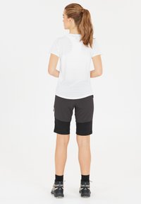 Lättviktig vit randig T-shirt med korta ärmar, kombinerad med svarta shorts. Shortsen har dragkedjefickor och olika tygsektioner.