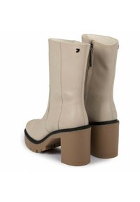 Botas de tobillo de cuero beige con un diseño texturizado, tacones cuadrados altos y cremalleras laterales. Acentos negros en el tobillo y la suela.