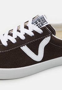 Baskets Vans en daim marron avec bande latérale en cuir blanc, lacets blancs et semelle en caoutchouc blanche, affichant le marquage de l'étiquette sur la languette.