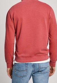 Rotes Sweatshirt aus Baumwolle mit rundem Ausschnitt, gerippten Bündchen und Saum, getragen über einem weißen T-Shirt, kombiniert mit blauen Jeans aus Denim.