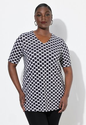 Tunic a maniche corte con scollatura a V in un motivo geometrico bianco e nero, caratterizzata da una vestibilità rilassata e una texture del tessuto liscia, abbinata a leggings neri.