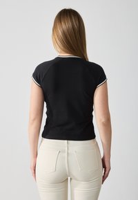 Black short-sleeve top with white trim, fitted design, and smooth texture. Worn with light-colored fitted pants, showcasing a simple style.