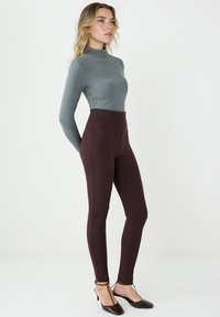 Szara bluzka z długim rękawem i półgolfem, zestawiona z wysokim stanem bordowych legginsów. Outfit charakteryzuje się dopasowanym krojem i gładką teksturą.