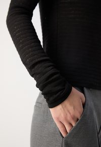 Černý top s dlouhým rukávem a žebrovanou texturou, zkombinovaný se šedými kalhotami s bočními kapsami. Zaměření na detaily tkaniny a střihu.