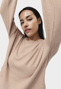 Žebrovaný, světle béžový svetr s dlouhými rukávy a kulatým výstřihem, vyrobený z měkké, texturované látky. Má pohodlný volný střih.