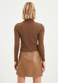 Top de cuello alto marrón acanalado combinado con una minifalda de cuero marrón que presenta un cierre central y un diseño entallado, visto desde atrás.