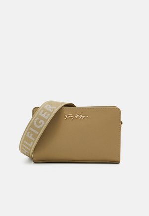 Brun rektangulær crossbody taske med bredt mærket skulderrem og lille metallisk Tommy Hilfiger-logo foran i midten.