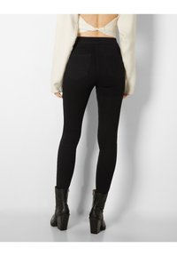 Zwarte skinny jeans met een hoge tailleband, voorzien van twee achterzakken. Draag ze met een witte crop top en zwarte enkellaarsjes.