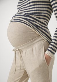 Beige graviditets joggebukser med snøring i livet og sidede lommer, kombinert med en mørk blå og kremfarget stripet ribbestrikket topp.