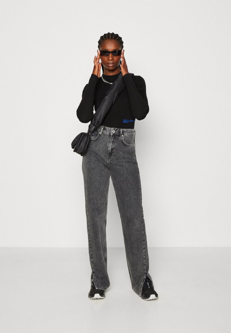 Haut noir à manches longues côtelé, jeans en denim gris taille haute, sac bandoulière noir, baskets noires et lunettes de soleil sombres. Design simple, coupe décontractée.