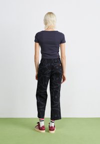 Pantaloni neri con un motivo di cerchi e linee, abbinati a una maglietta scura aderente. Mantenuti con calze a righe rosse e bianche e scarpe borgogna.