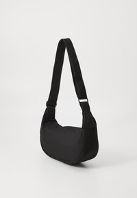 Borsa a spalla nera realizzata in materiale morbido, con una forma curva e una tracolla spessa con branding in rilievo. Superficie liscia e design minimal.