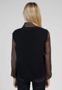 Pull sans manches en maille bleu marine avec une texture côtelée, porté sur une chemise à manches longues marron, avec un col arrondi et un ourlet ajusté.