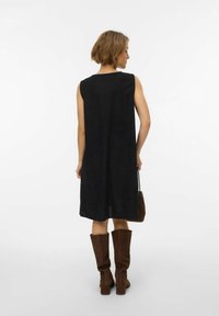 Melna bezroku kleita ar brīvu piegriezumu, ceļgalu garuma dizains, mīksta tekstūra, papildināta ar brūnām ceļgalu augstuma zamšādas zābakiem un mazu somiņu.