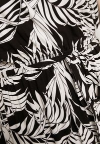 Sort og hvidt kjolestof med et bladmønster, der har en elastisk talje og et bundet stofbælte.