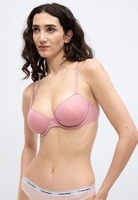Ροζ επενδυμένο σουτιέν με ρυθμιζόμενους ιμάντες, χαρακτηριστικό ομαλής υφής και κλασικού σχεδιασμού. Λογότυπο Calvin Klein στη ζώνη των αντίστοιχων εσωρούχων.