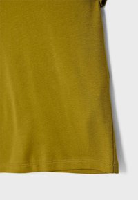 T-shirt verde oliva con una texture morbida, orlo arrotondato e cuciture visibili nella parte inferiore, che mostra un design semplice e casual.