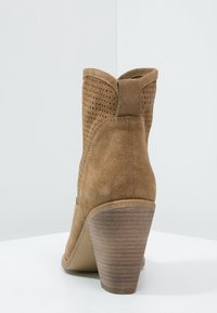 Stivale alla caviglia in suede marrone con un design perforato testurizzato, linea superiore curvata e tacco in legno impilato.