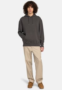 Felpa grigia con cappuccio e tasca frontale, abbinata a pantaloni beige e scarpe marroni. Presenta stringhe nel cappuccio e una vestibilità comoda.