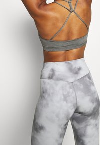 Achteraanzicht van een persoon die een grijze sportbh met bandjes en een grijze leggings met hoge taille en tie-dye patroon draagt tegen een effen achtergrond.