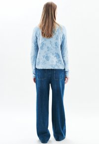Jasnoniebieski sweter w kwiatowy wzór, uszyty z miękkiego materiału, w połączeniu z luźnymi, ciemnoniebieskimi dżinsami z tylnymi kieszeniami.