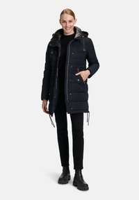 Giacca parka nera imbottita con cappuccio foderato in pelliccia sintetica, chiusura con zip, due tasche laterali e dettagli con coulisse in vita.