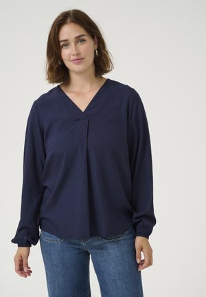 Marineblaues, langärmeliges Bluse aus leichtem, strukturiertem Stoff mit V-Ausschnitt und gerafften Ärmeln, kombiniert mit Jeans.