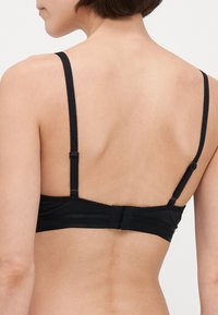 Mustmust, millel on reguleeritavad rihmad, küpsiste ja silmade sulgemisseade ning sile tekstuur koos lihtsa disainiga, millel ei ole lisamustreid.