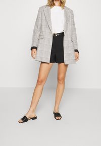 Černobílé kárované oversize sako, bílé texturované tričko, černé šortky s vysokým pasem a černé sandály s nízkým podpatkem.