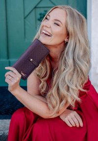 Purple leather wallet with textured surface, gold hardware, and a decorative logo. Positioned against a teal background.