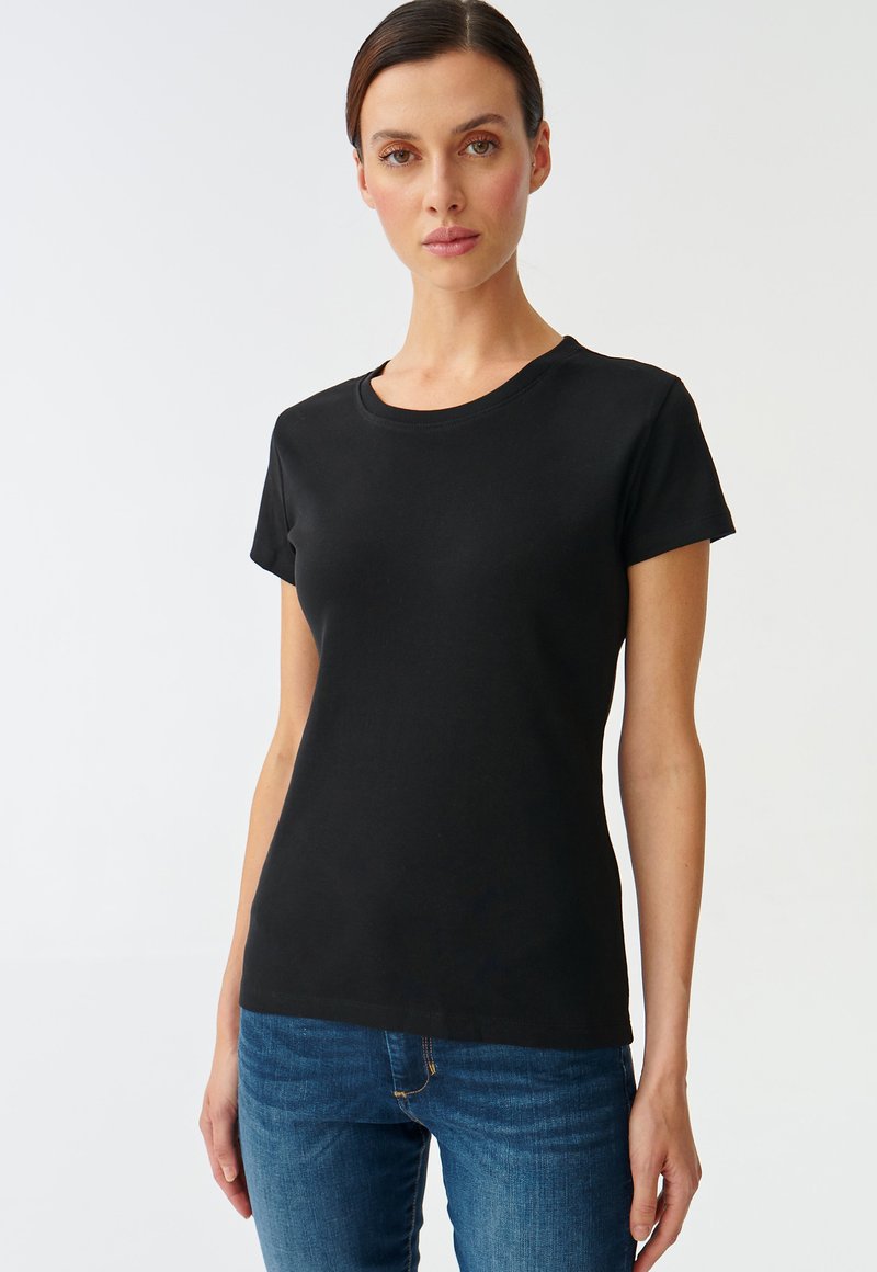 T-shirt nera a maniche corte in cotone, con scollo rotondo e design aderente. Abbinata a jeans blu.