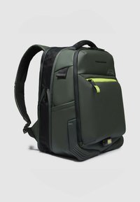 Mochila impermeable verde con detalles en negro, correas acolchadas, bolsillo frontal con cremallera y compartimento inferior con luz. Textura lisa.