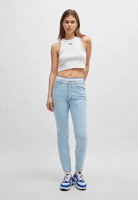 Bela kratka majica brez rokavov in svetlo modre ozke kavbojke. Superge z modrimi in črnimi poudarki. Minimalističen dizajn, gladka tekstura.