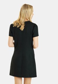 Vestido negro de manga corta con un diseño ajustado, que presenta una textura suave y un sutil detalle de costura en la parte posterior.