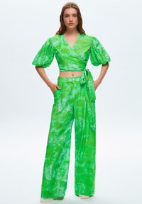 Groene, geblokte wikkeltop met pofmouwen, gecombineerd met hoog in de taille zittende, wijde broeken. Het materiaal lijkt lichtgewicht en textuur te hebben.