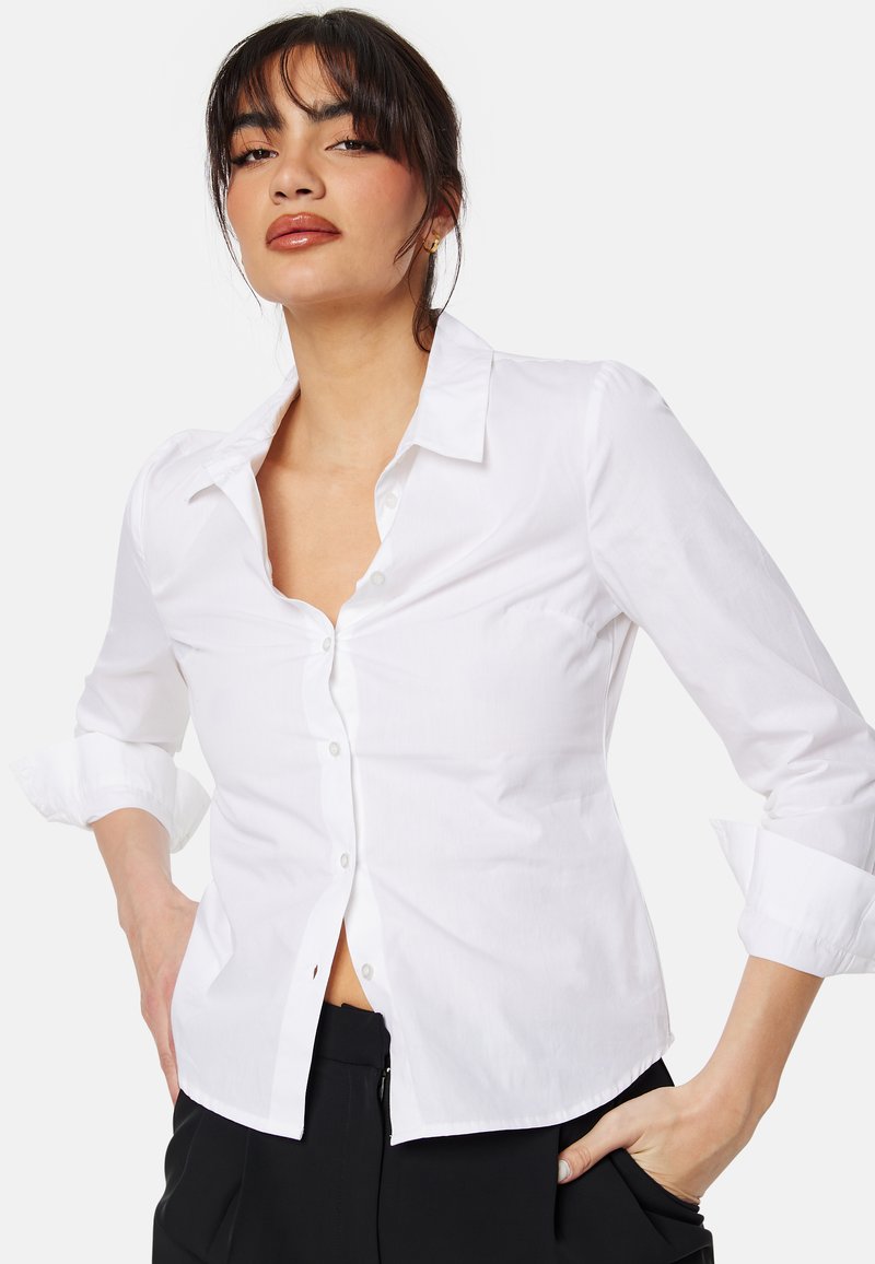 Camicia bianca con colletto, design aderente, maniche lunghe arrotolate, caratterizzata da una texture liscia e da un dettaglio minimale.