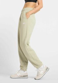 Light green jogger pants with elastic waistband and side pockets. Paired with beige and white sneaker featuring a subtle logo.