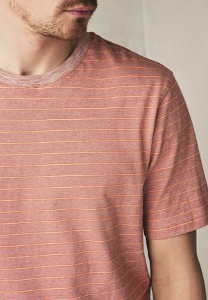 Man wearing short-sleeve, crew-neck T-shirt with thin horizontal red and orange stripes against neutral background.