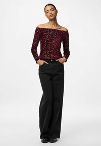 Burgunderfarvet bluse uden skuldre med pailletter, lange ærmer og tætsiddende design, parret med højtaljede sorte bukser med vidde og sorte sko.