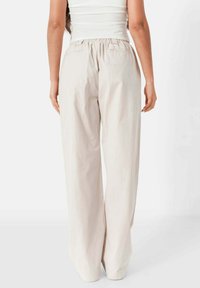 Beige wijde broek met een elastische tailleband, gemaakt van een zachte, lichte stof. Heeft een eenvoudig ontwerp en geen zichtbare logo's of patronen.