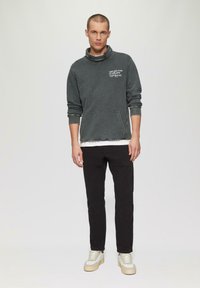 Donkergrijze sweatshirt met hoge kraag, voorzak en bedrukte ontwerpen. Gecombineerd met zwarte broek en beige sneakers. Eenvoudige, relaxte pasvorm.