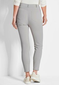 Lichtgrijze stretchbroek met een slim fit, voorzien van achterzakken en een zachte textuur, gecombineerd met off-white sneakers.