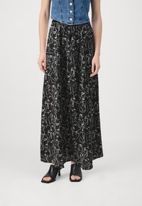 Jupe maxi noire avec un motif de lignes abstraites blanches, taille élastique, associée à un top en denim court et des talons ouverts noirs.