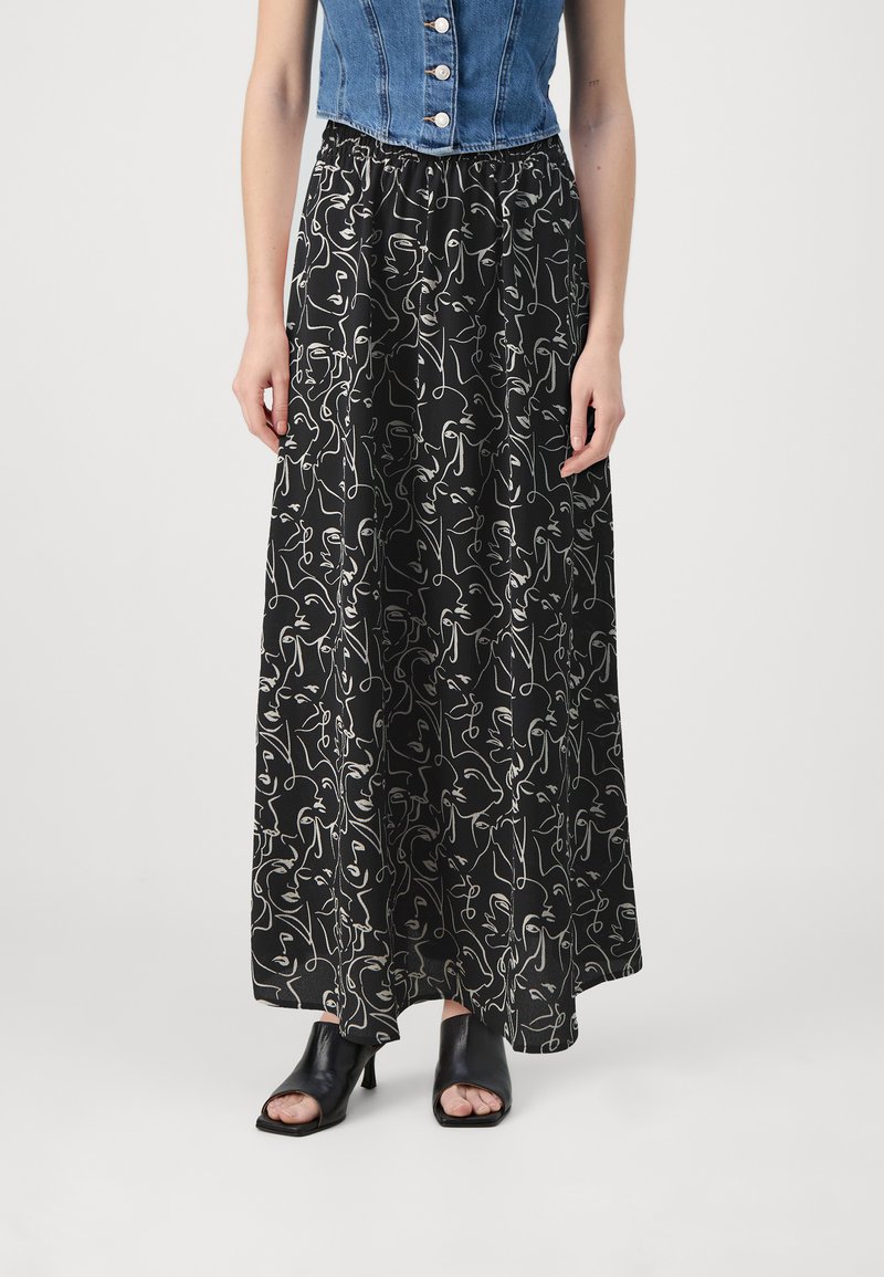 Jupe maxi noire avec un motif de lignes abstraites blanches, taille élastique, associée à un top en denim court et des talons ouverts noirs.