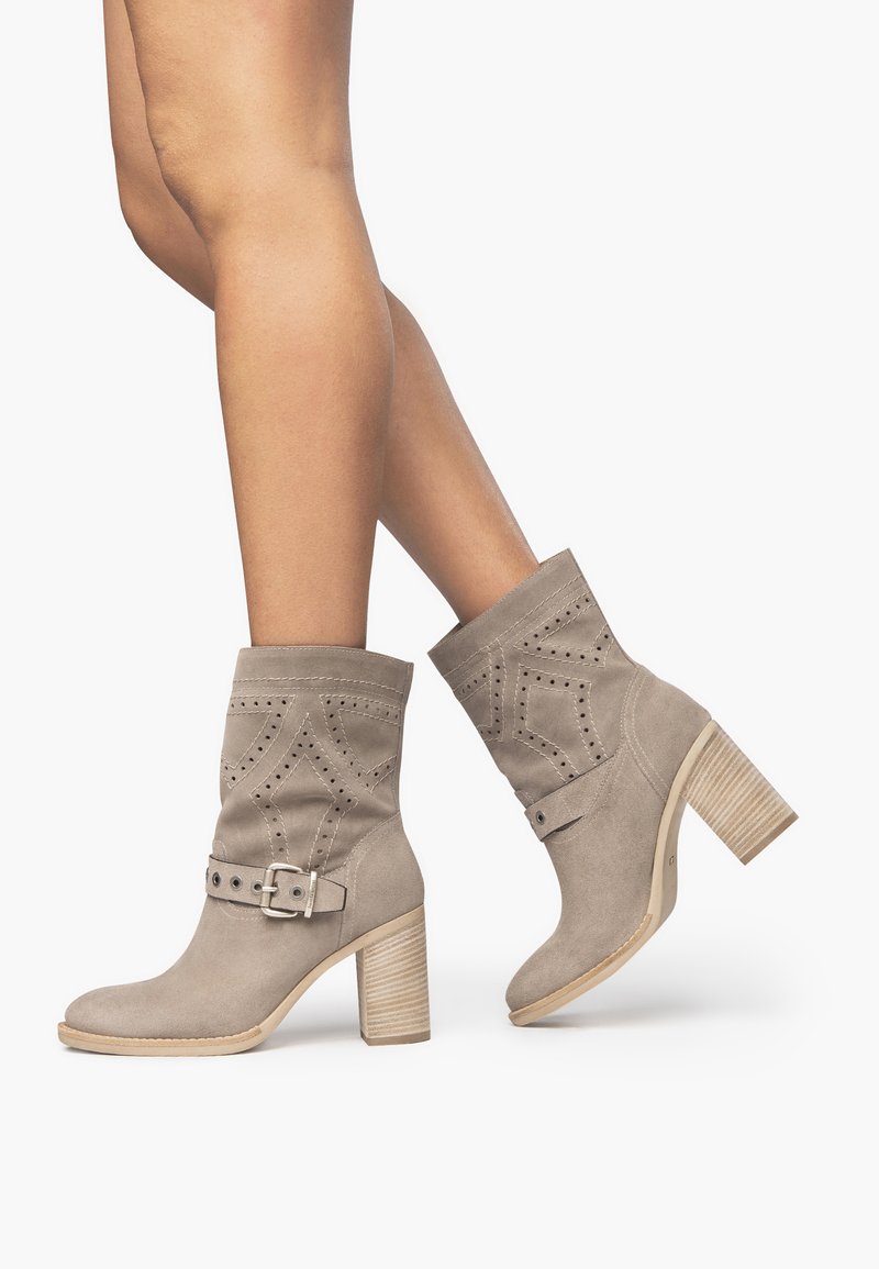 Beige Wildleder-Stiefeletten mit einem breiten strukturierten Absatz, dekorativen durchbrochenen Mustern und einem verstellbaren Schnallenriemen im oberen Abschnitt.
