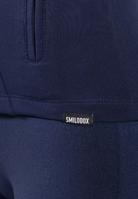 Leggings deportivos de color azul marino fabricados en una tela suave. Cuentan con un bolsillo lateral y una etiqueta negra que dice "SMILODOX". La textura es uniforme en toda la prenda.