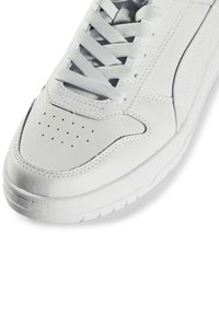Empiècement avant de sneaker en cuir blanc avec surface texturée, perforations, lacets plats blancs et détails cousus sur fond blanc.