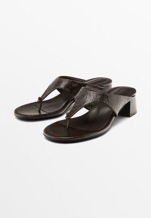 Brown leather sandals with a T-strap design, textured finish, and a low block heel, featuring a circular accent at the center.
